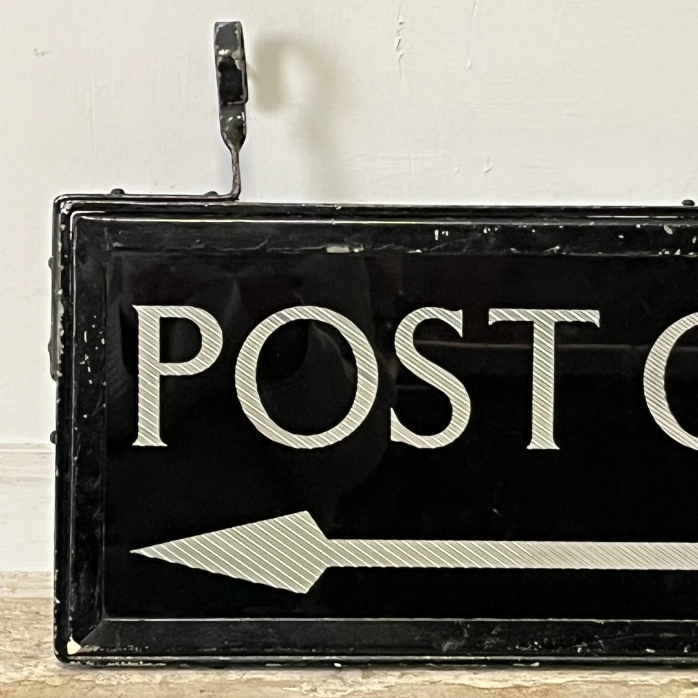 A rectangular double-sided black glass directional sign featuring white lettering that reads POST OFFICE above a striped directional arrow, mounted in a dark iron frame with top loops. View III
