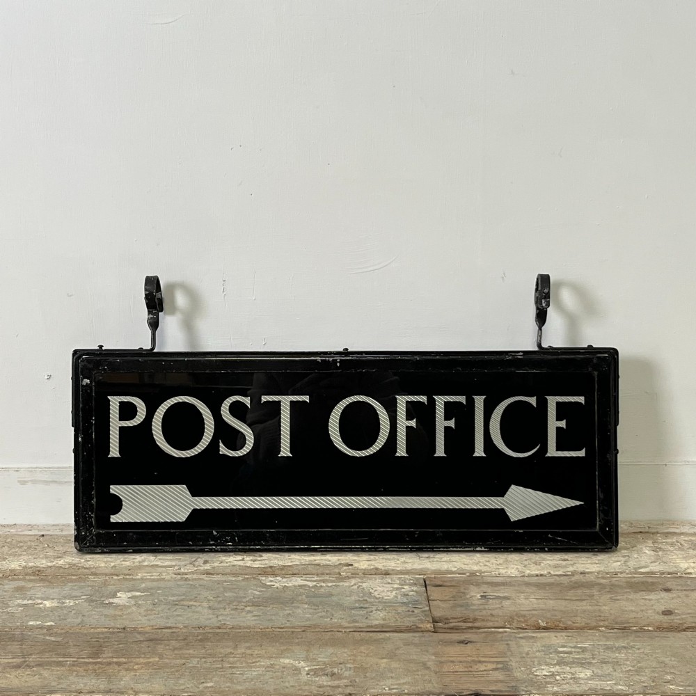 A rectangular double-sided black glass directional sign featuring white lettering that reads POST OFFICE above a striped directional arrow, mounted in a dark iron frame with top loops. View IV