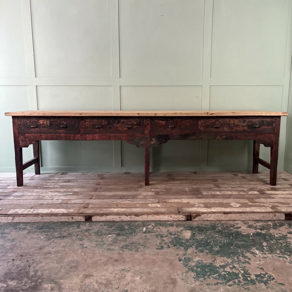 An early 19th-century pine serving table featuring a natural scrubbed timber top and a dark painted base with six legs and four drawers.