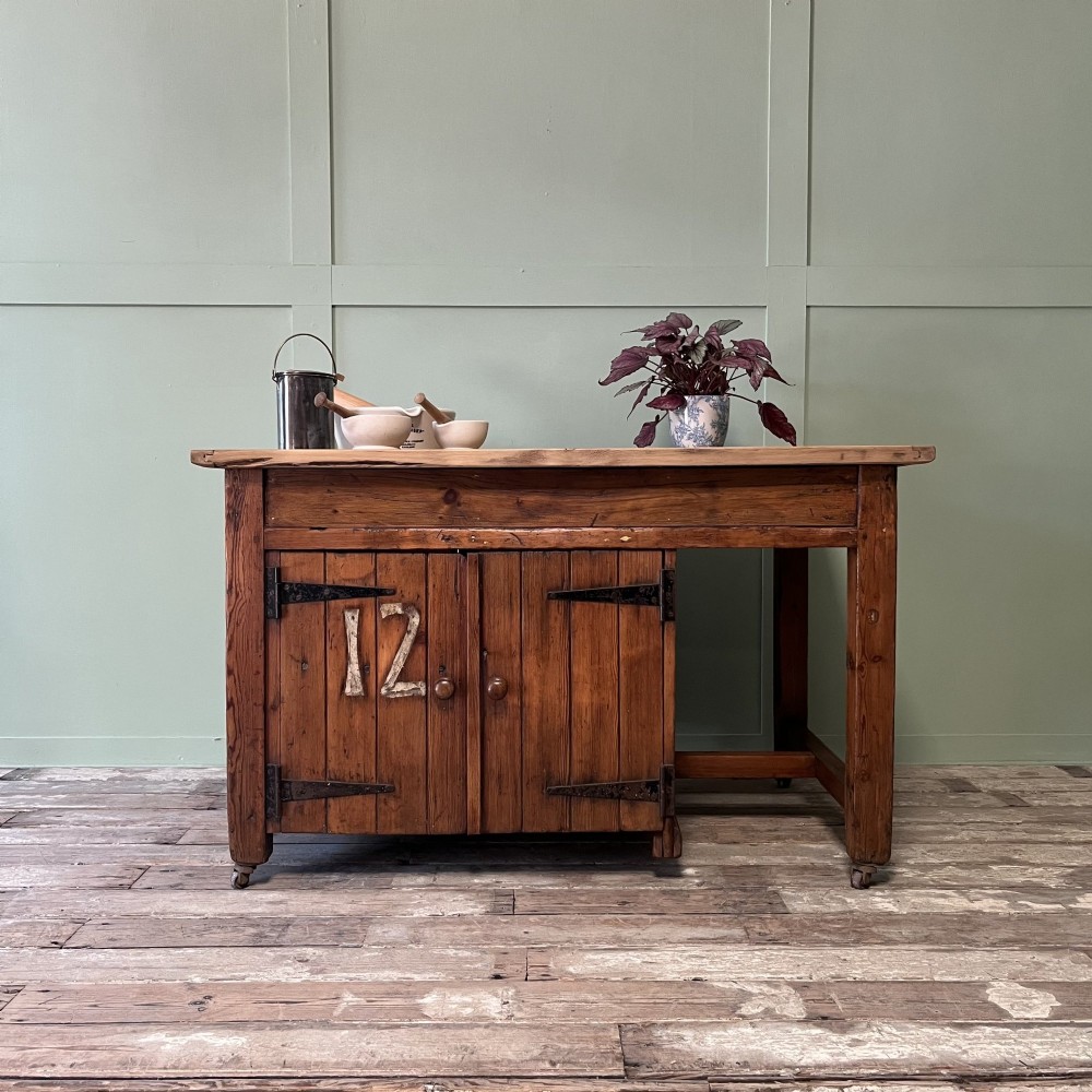 An early twentieth-century rustic pine bakers prep table with dual cupboard doors, black iron strap hinges, painted number twelve, and wooden castors.