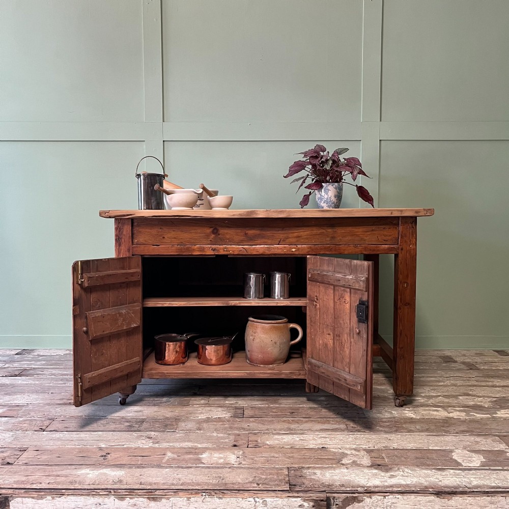 An early twentieth-century rustic pine bakers prep table with dual cupboard doors, black iron strap hinges, painted number twelve, and wooden castors. View II