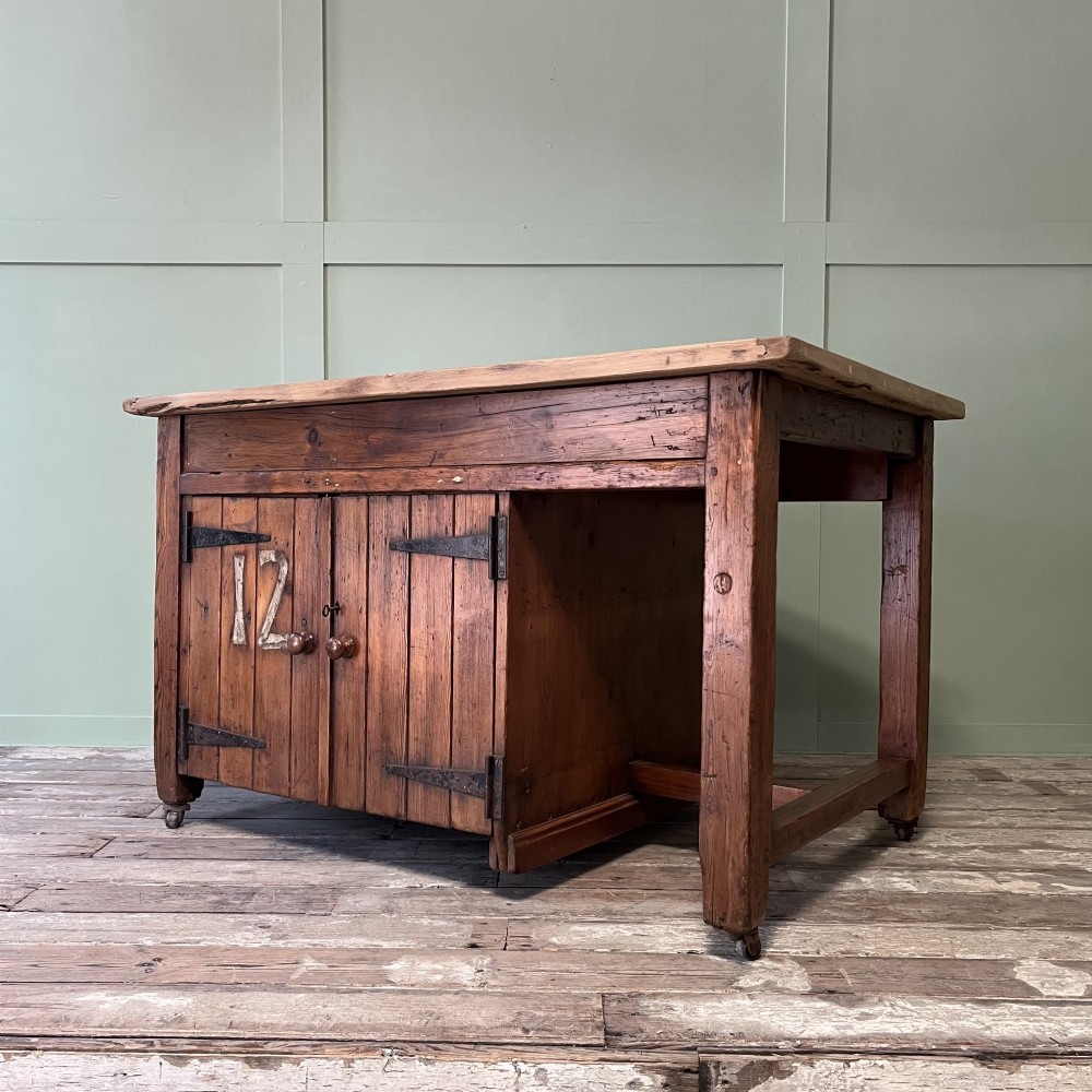 An early twentieth-century rustic pine bakers prep table with dual cupboard doors, black iron strap hinges, painted number twelve, and wooden castors. View III