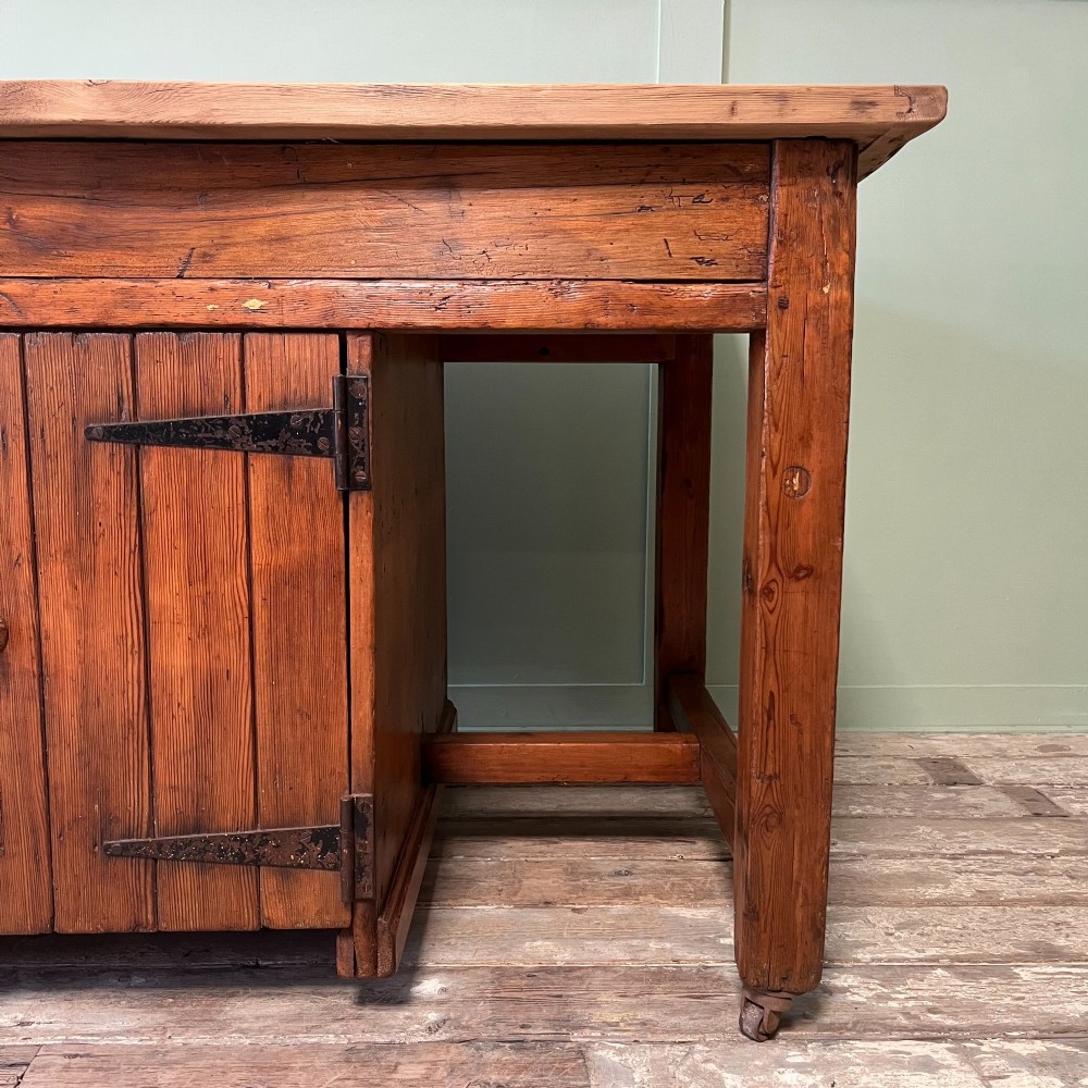 An early twentieth-century rustic pine bakers prep table with dual cupboard doors, black iron strap hinges, painted number twelve, and wooden castors. View VI