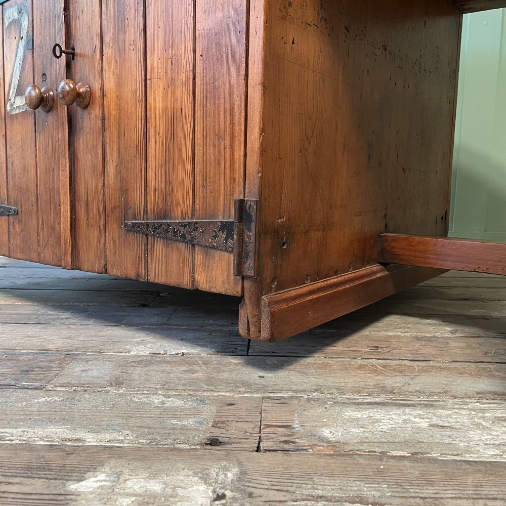 An early twentieth-century rustic pine bakers prep table with dual cupboard doors, black iron strap hinges, painted number twelve, and wooden castors. View VII