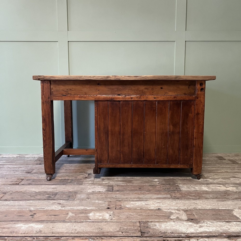 An early twentieth-century rustic pine bakers prep table with dual cupboard doors, black iron strap hinges, painted number twelve, and wooden castors. View X