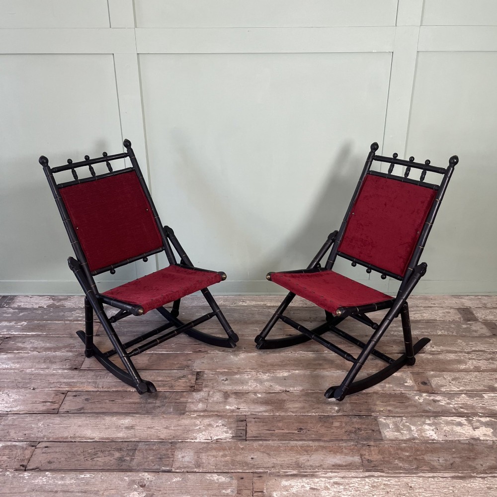 A pair of Victorian ebonised wood folding rocking chairs featuring faux bamboo turned frames and deep red velvet upholstered seats and backrests. View II