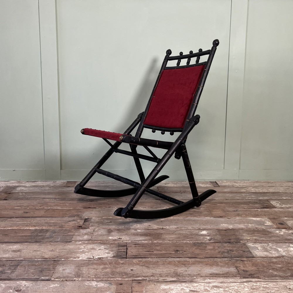 A pair of Victorian ebonised wood folding rocking chairs featuring faux bamboo turned frames and deep red velvet upholstered seats and backrests. View III
