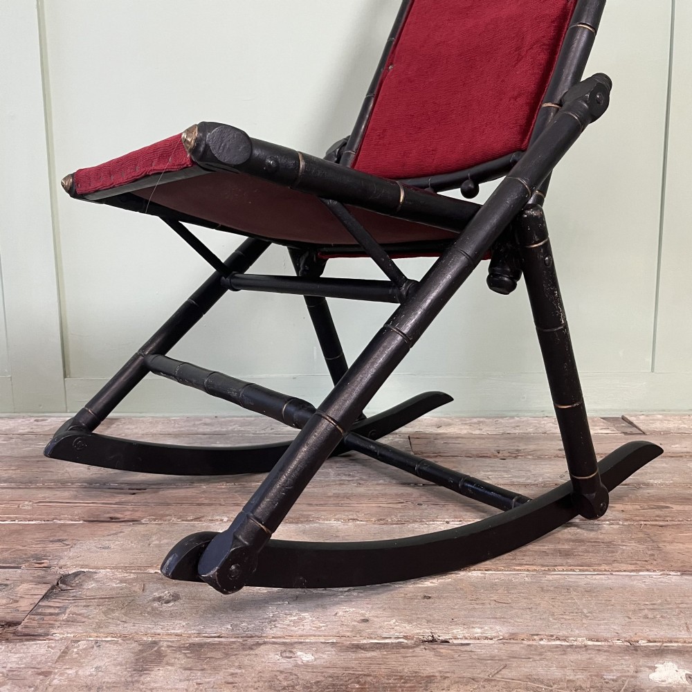 A pair of Victorian ebonised wood folding rocking chairs featuring faux bamboo turned frames and deep red velvet upholstered seats and backrests. View IV