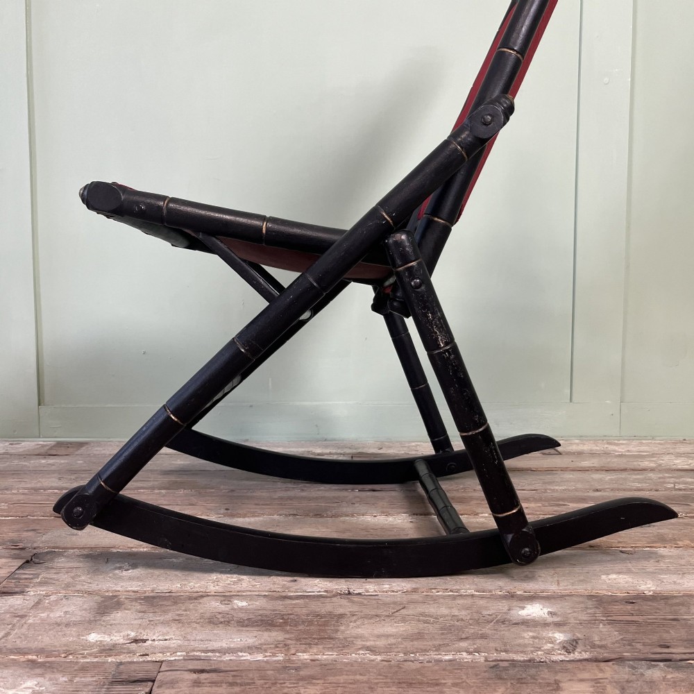 A pair of Victorian ebonised wood folding rocking chairs featuring faux bamboo turned frames and deep red velvet upholstered seats and backrests. View V