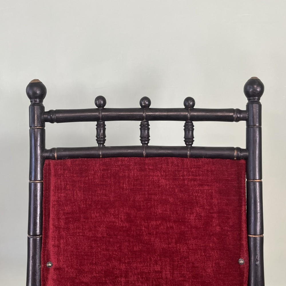 A pair of Victorian ebonised wood folding rocking chairs featuring faux bamboo turned frames and deep red velvet upholstered seats and backrests. View VIII