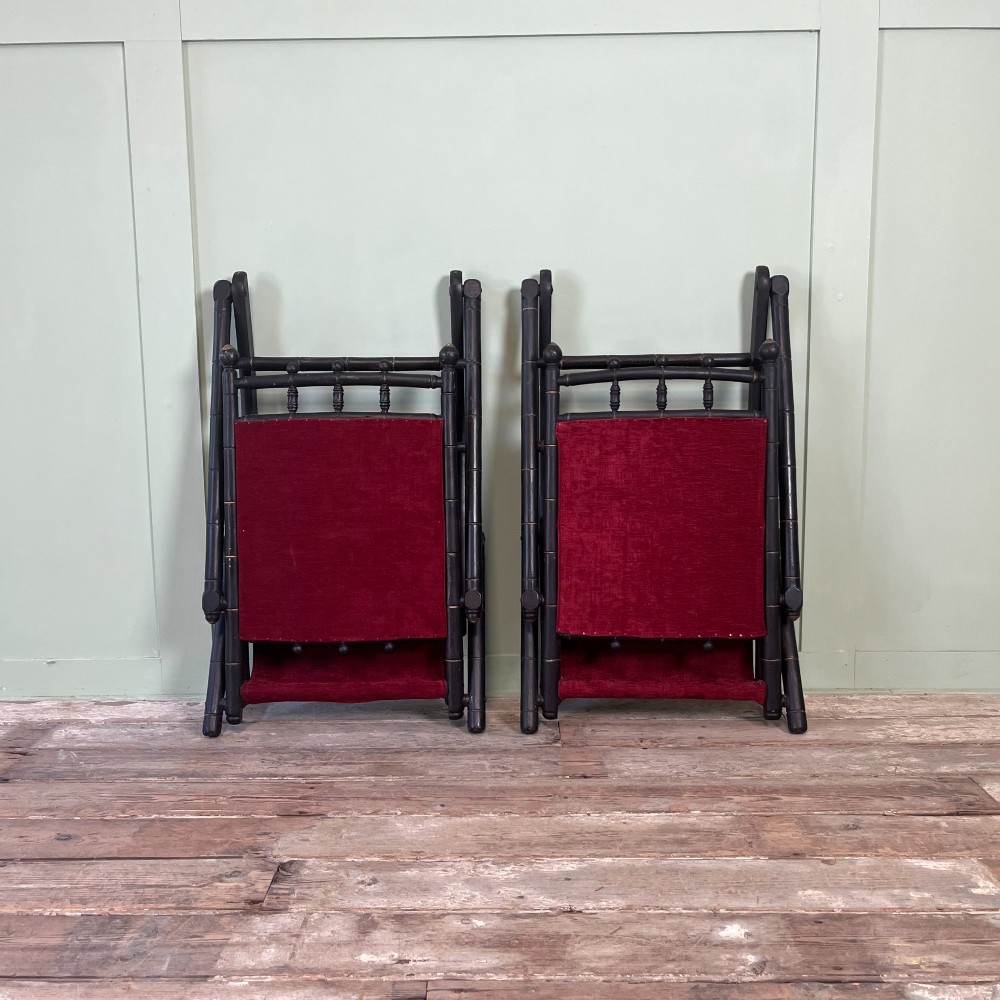 A pair of Victorian ebonised wood folding rocking chairs featuring faux bamboo turned frames and deep red velvet upholstered seats and backrests. View XIV