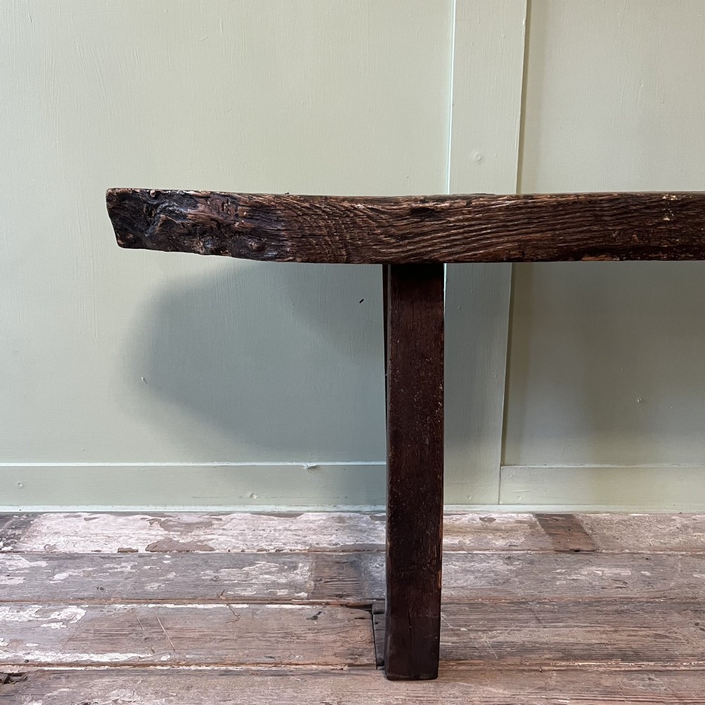 A long rustic dark oak bench featuring an unrefined thick slab seat supported by four simple splayed legs. View III