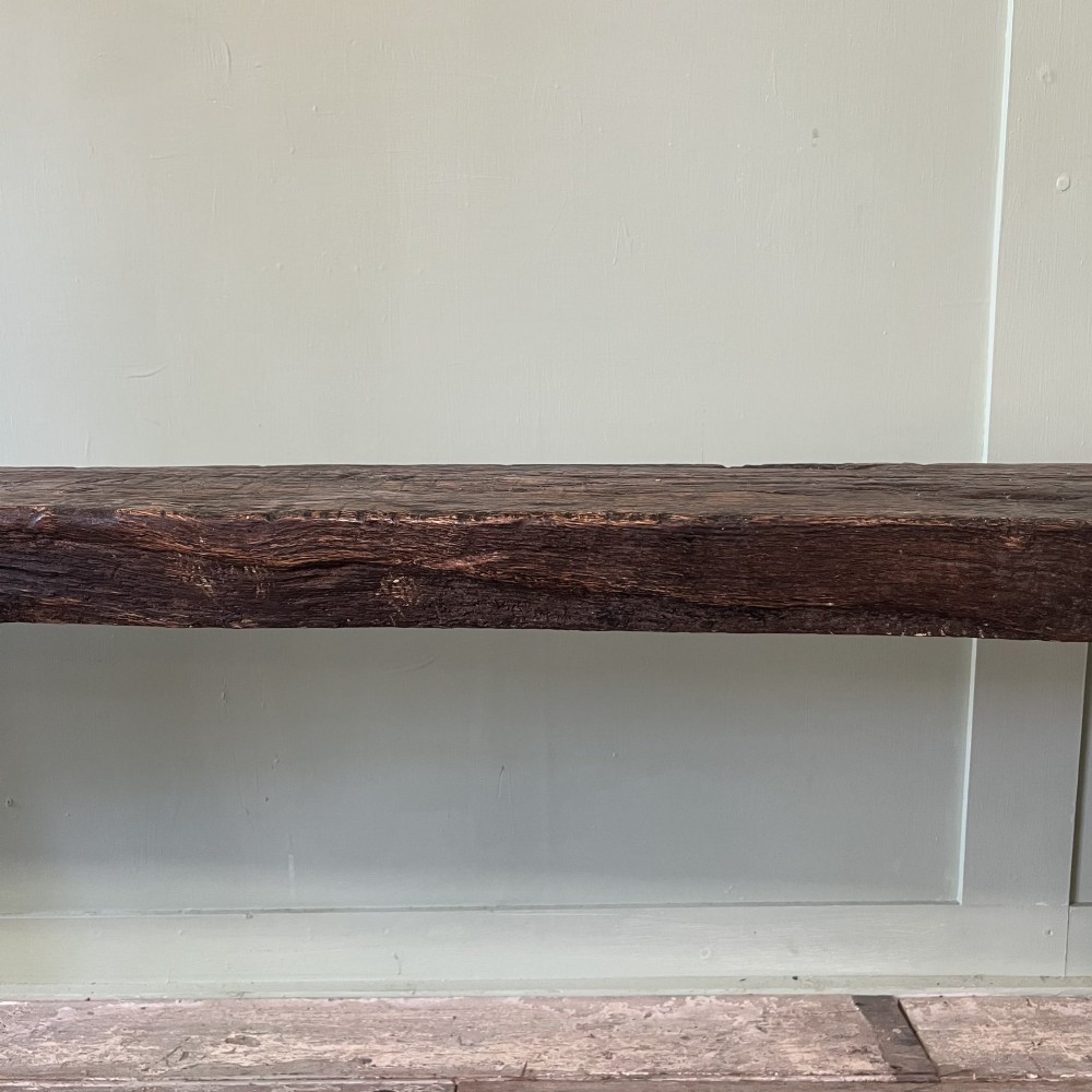 A long rustic dark oak bench featuring an unrefined thick slab seat supported by four simple splayed legs. View IV