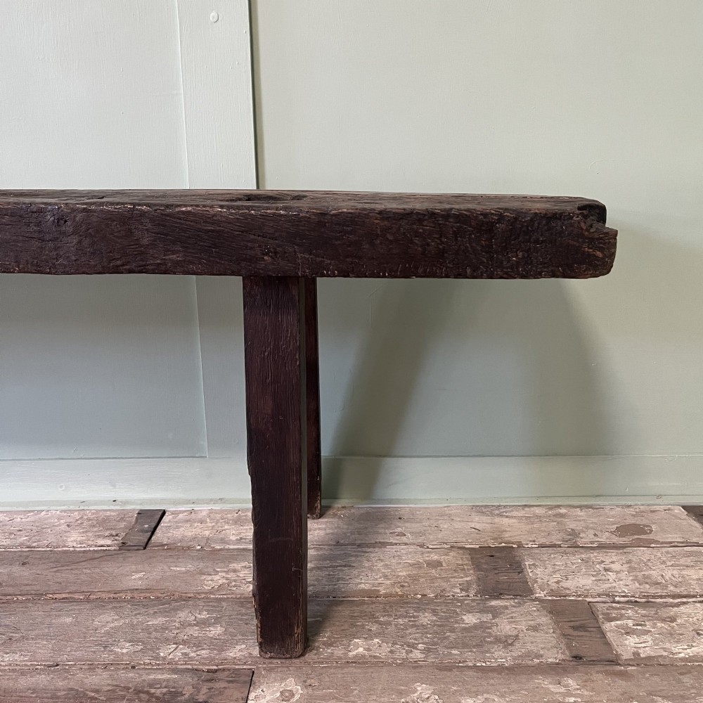 A long rustic dark oak bench featuring an unrefined thick slab seat supported by four simple splayed legs. View V