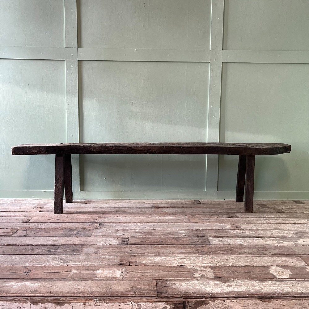 A long rustic dark oak bench featuring an unrefined thick slab seat supported by four simple splayed legs. View XII