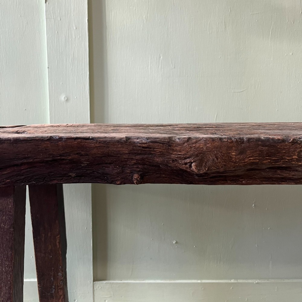 A long rustic dark oak bench featuring an unrefined thick slab seat supported by four simple splayed legs. View XIV