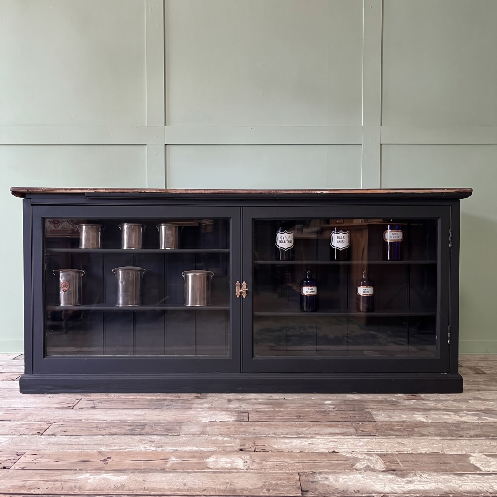 A Victorian shop counter featuring a dark painted pine base with two large glass panel doors and a polished mahogany top surface.