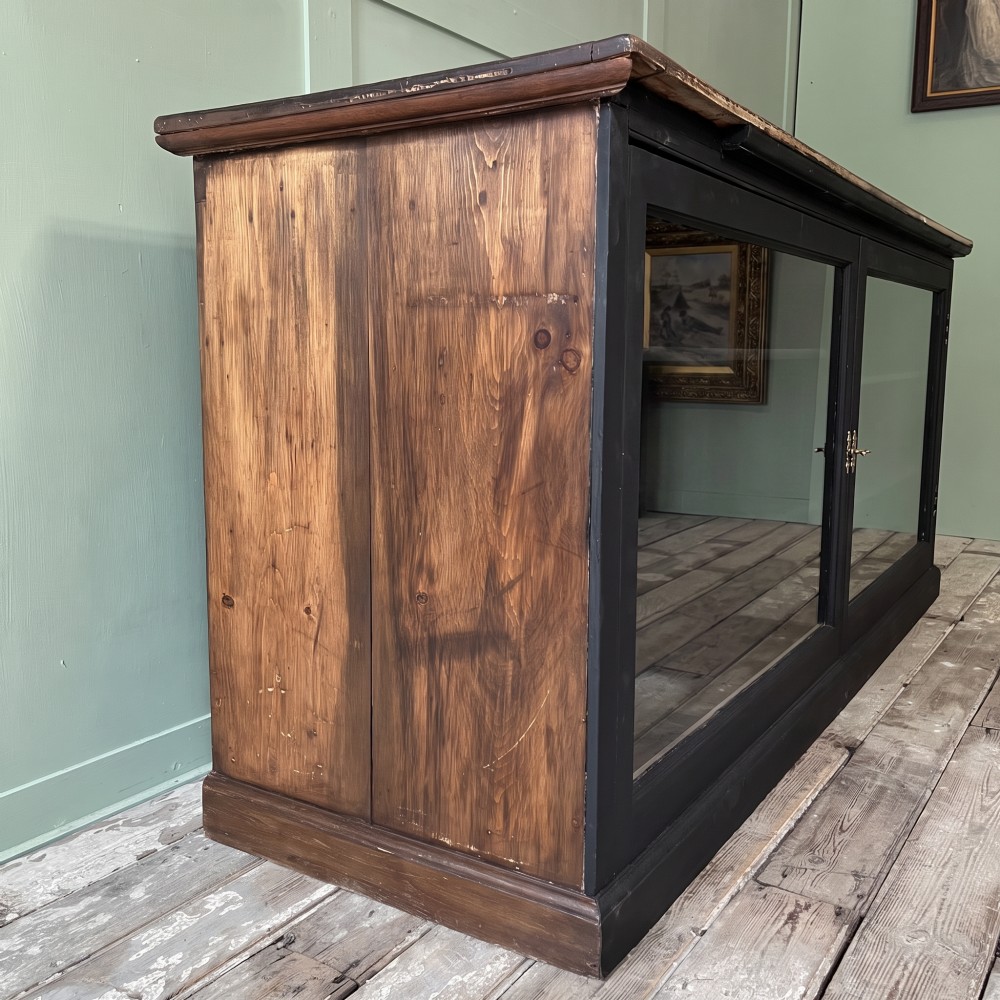 A Victorian shop counter featuring a dark painted pine base with two large glass panel doors and a polished mahogany top surface. View VI