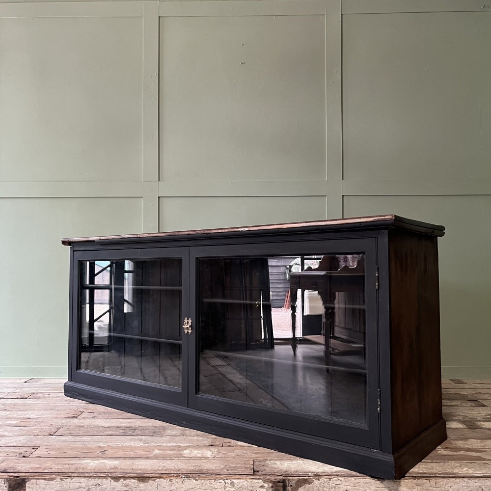 A Victorian shop counter featuring a dark painted pine base with two large glass panel doors and a polished mahogany top surface. View IX