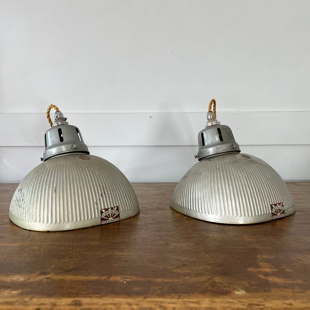 A pair of silver ribbed angled aluminium pendant light shades with vented gallery tops and twisted flex.