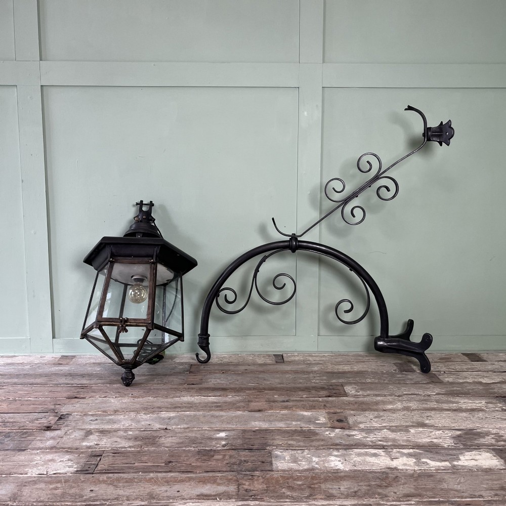 A pair of large metal street lanterns with glazed glass panels alongside two large decorative scrolled wrought iron wall brackets. View II