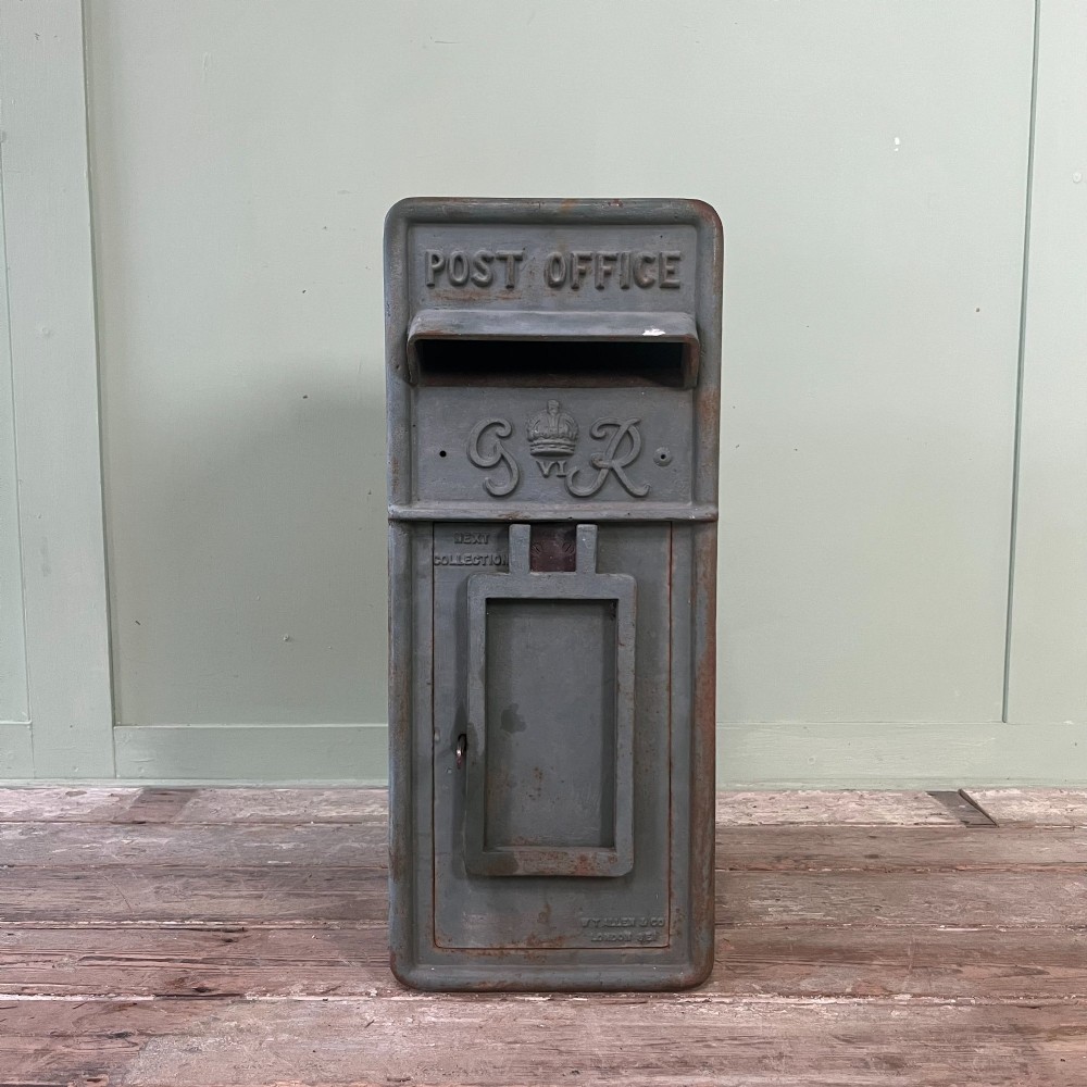 A cast iron George VI post box with a raised GR Royal cypher alongside a tall matching metal pedestal stand. View II