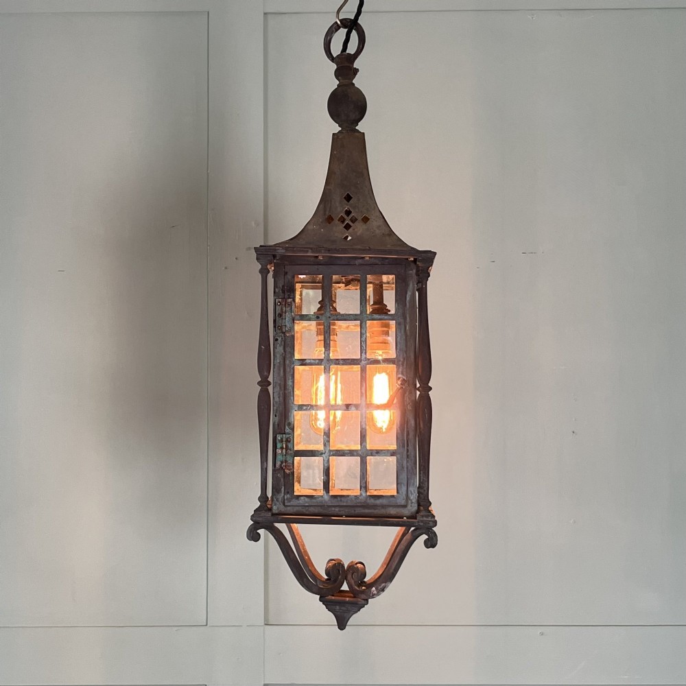 An Edwardian rectangular brass hanging lantern light fixture with glazed window panels, internal bulb fittings, a pagoda top, and a lower scroll finial.