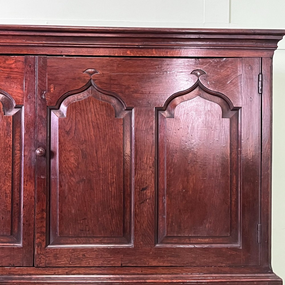 An 18th-century dark oak low linen press cupboard featuring arched fielded panel doors over a base with four drawers and brass handles. View VII