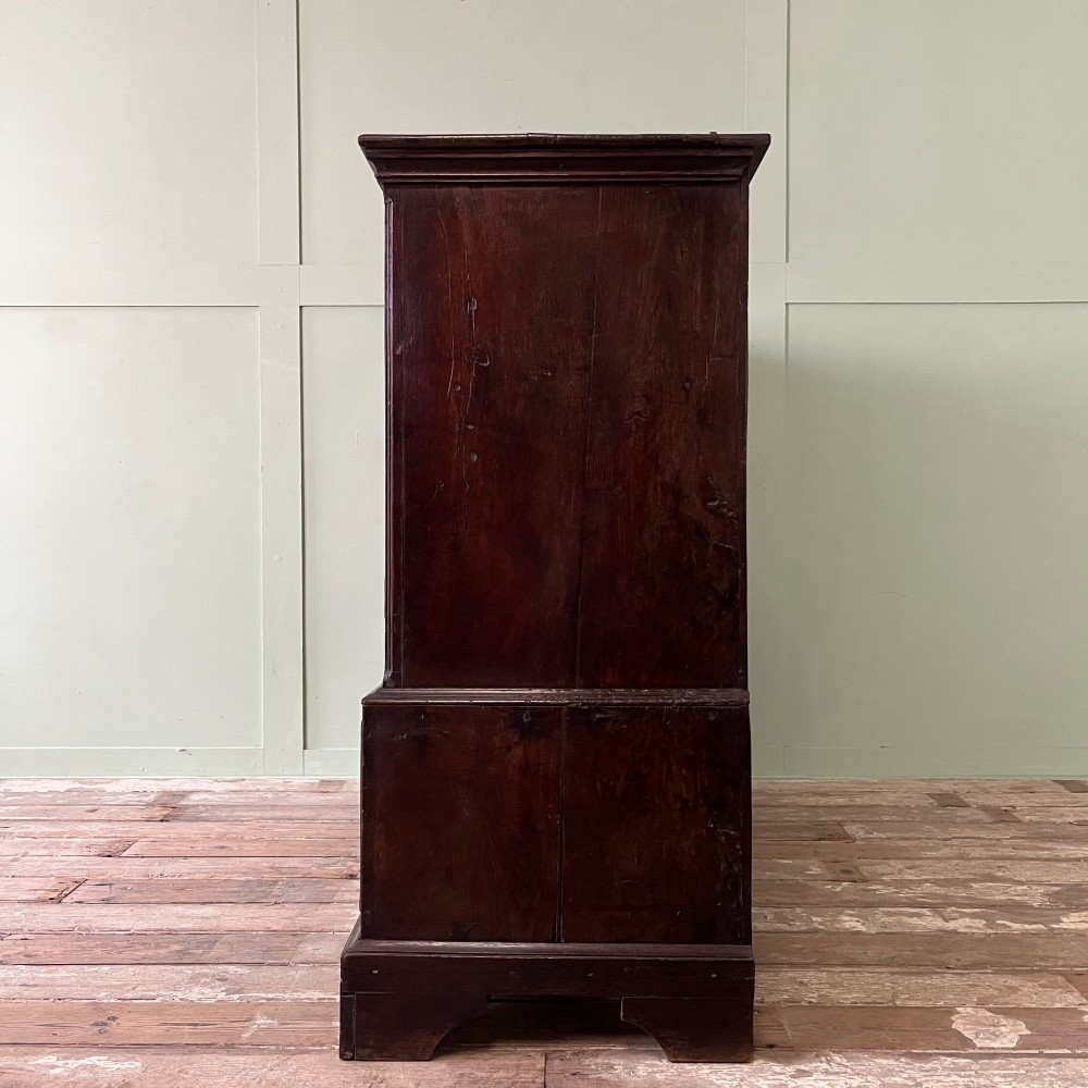 An 18th-century dark oak low linen press cupboard featuring arched fielded panel doors over a base with four drawers and brass handles. View VIII