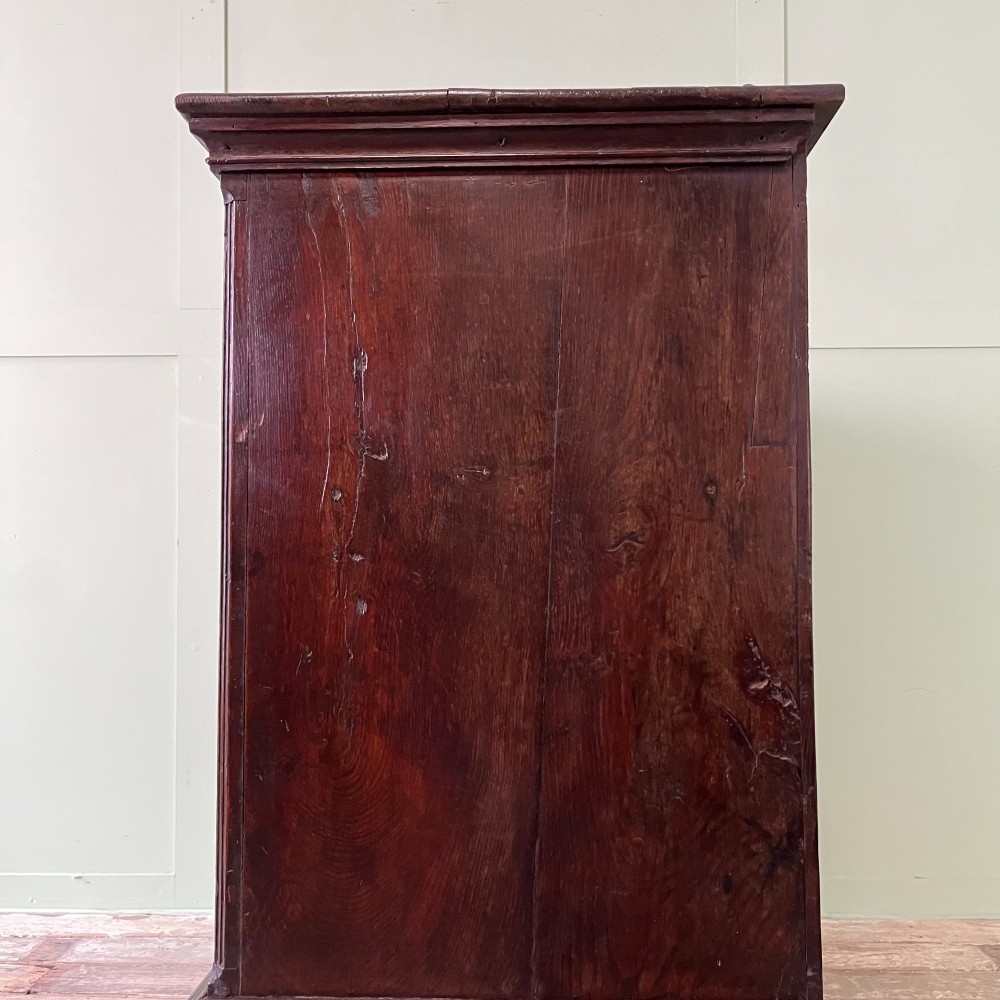 An 18th-century dark oak low linen press cupboard featuring arched fielded panel doors over a base with four drawers and brass handles. View X