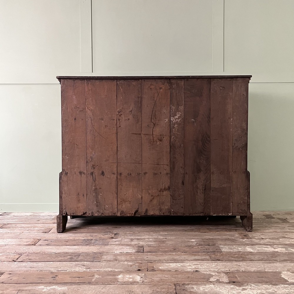 An 18th-century dark oak low linen press cupboard featuring arched fielded panel doors over a base with four drawers and brass handles. View XI