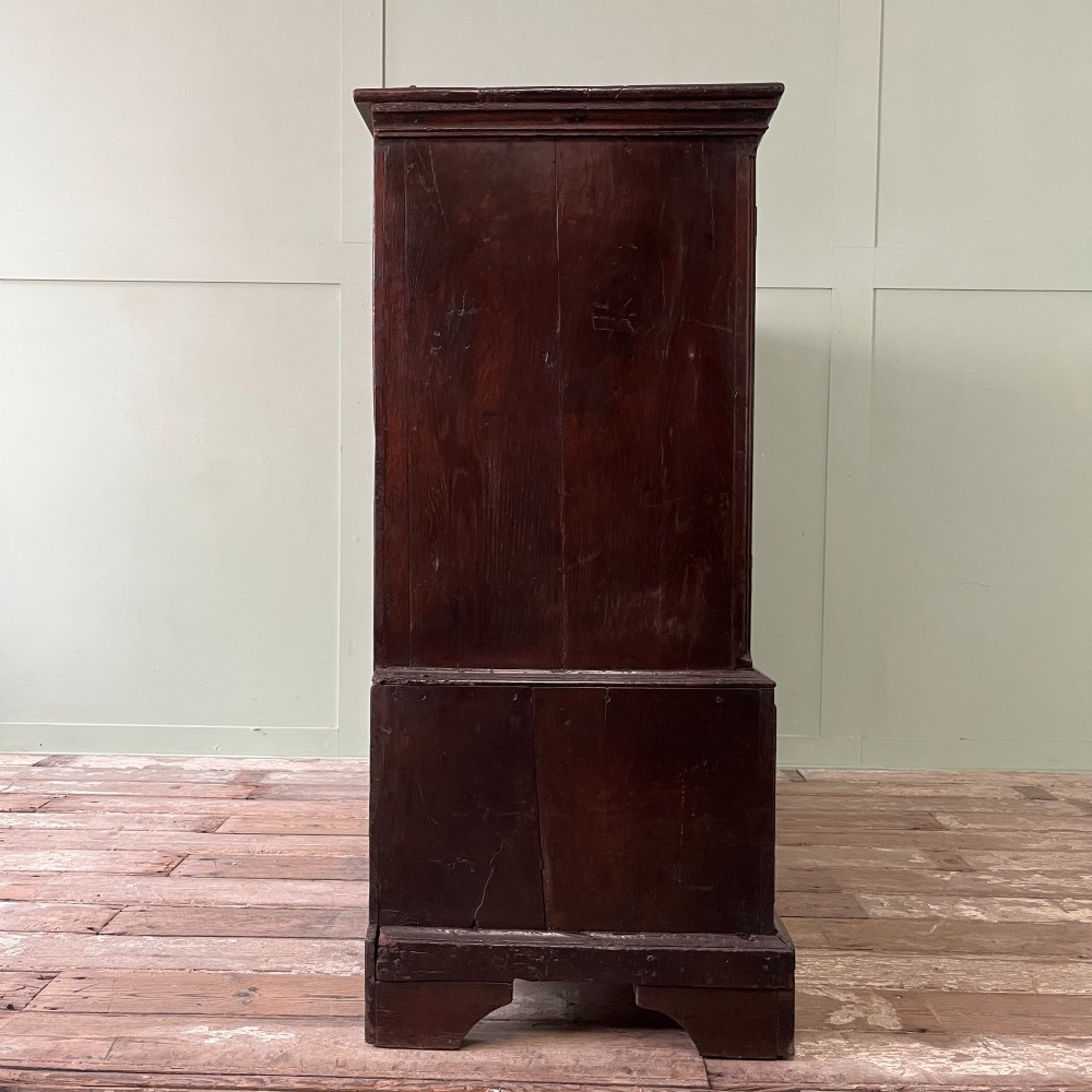 An 18th-century dark oak low linen press cupboard featuring arched fielded panel doors over a base with four drawers and brass handles. View XII