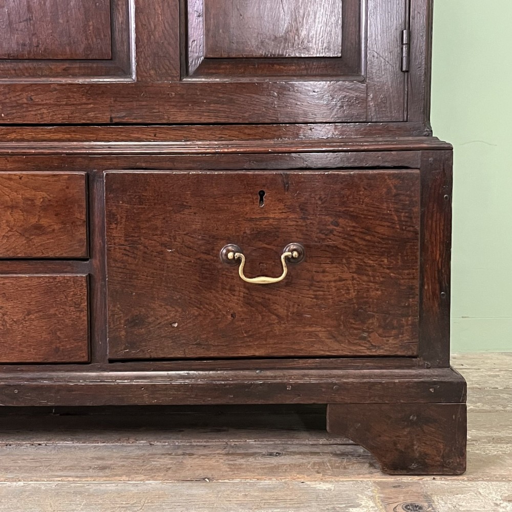 An 18th-century dark oak low linen press cupboard featuring arched fielded panel doors over a base with four drawers and brass handles. View XIV