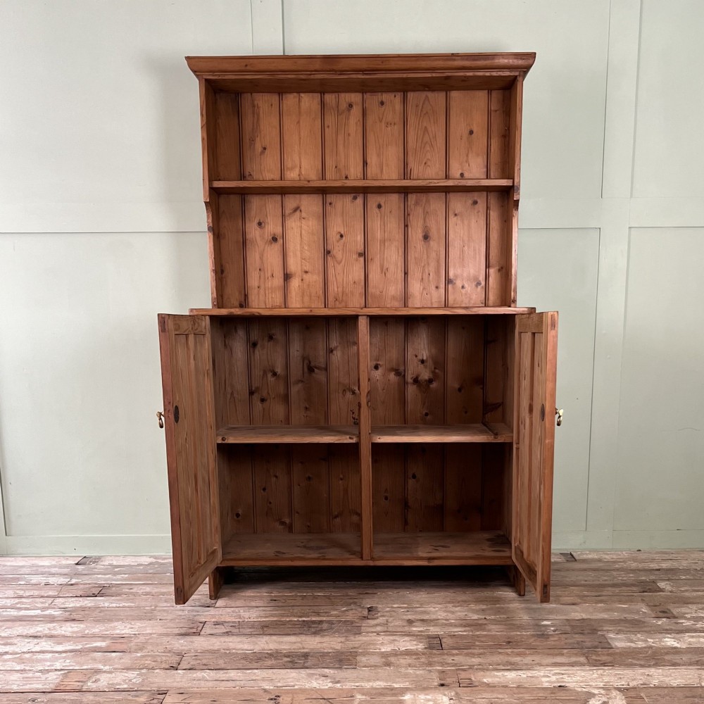 An early twentieth-century pine kitchen dresser featuring an open top display rack with two shelves above a two-door cabinet base with brass ring handles. View II