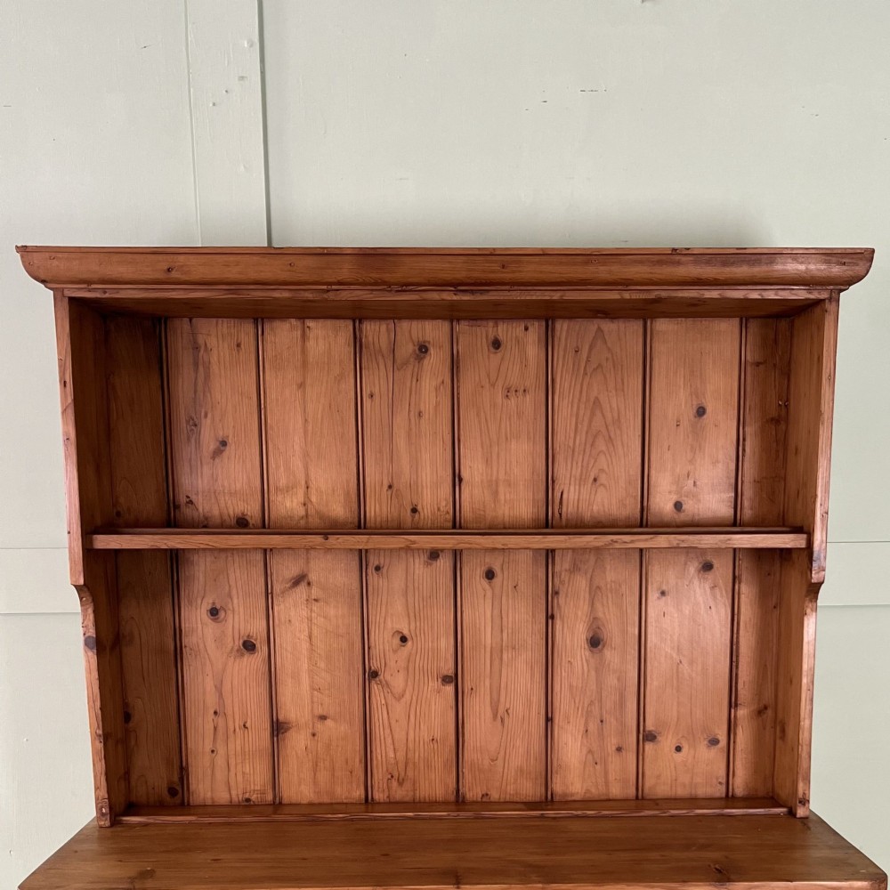 An early twentieth-century pine kitchen dresser featuring an open top display rack with two shelves above a two-door cabinet base with brass ring handles. View III