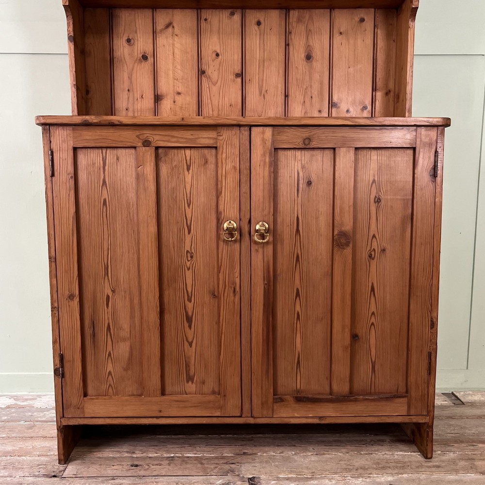 An early twentieth-century pine kitchen dresser featuring an open top display rack with two shelves above a two-door cabinet base with brass ring handles. View IV