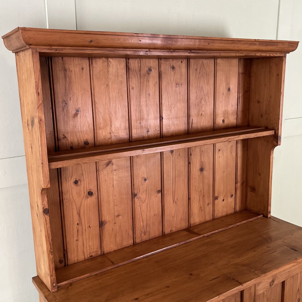 An early twentieth-century pine kitchen dresser featuring an open top display rack with two shelves above a two-door cabinet base with brass ring handles. View V