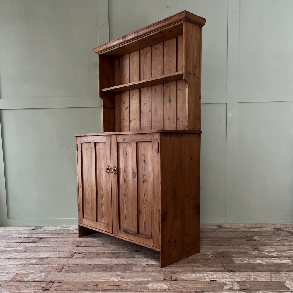An early twentieth-century pine kitchen dresser featuring an open top display rack with two shelves above a two-door cabinet base with brass ring handles. View VI