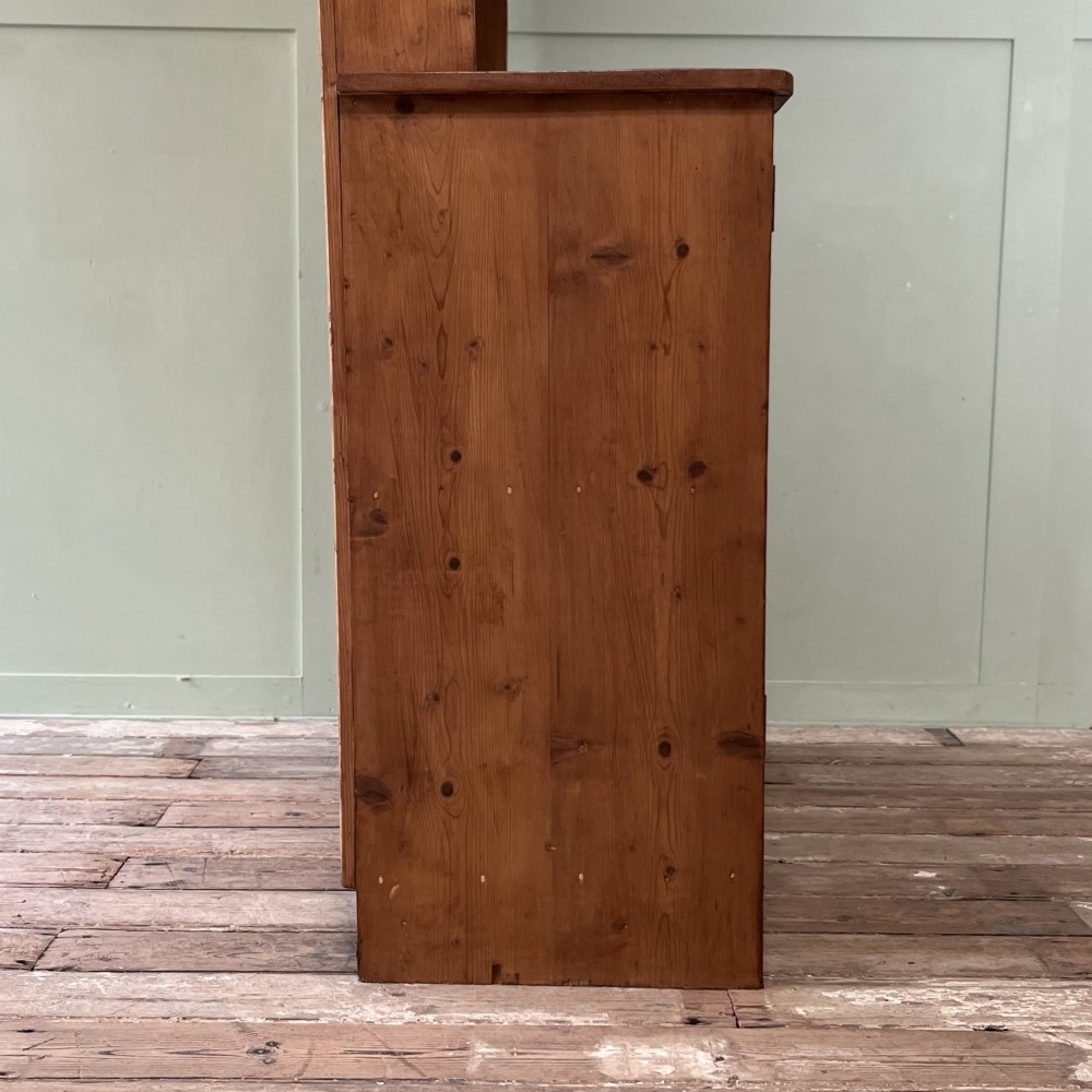 An early twentieth-century pine kitchen dresser featuring an open top display rack with two shelves above a two-door cabinet base with brass ring handles. View X