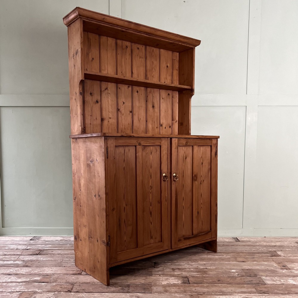 An early twentieth-century pine kitchen dresser featuring an open top display rack with two shelves above a two-door cabinet base with brass ring handles. View XI