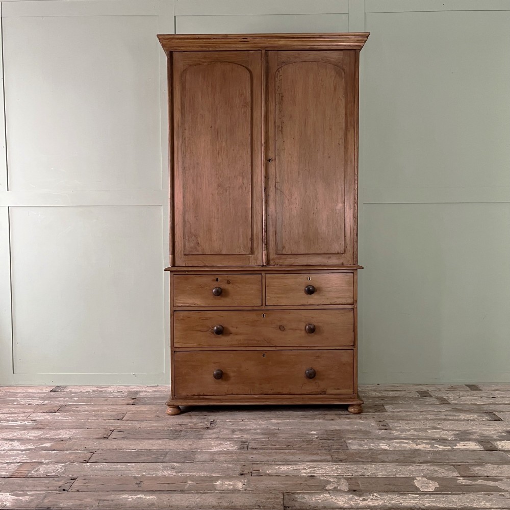 An antique Victorian pine cupboard on chest featuring a top section with two arched panel doors above three drawers with turned wooden handles.