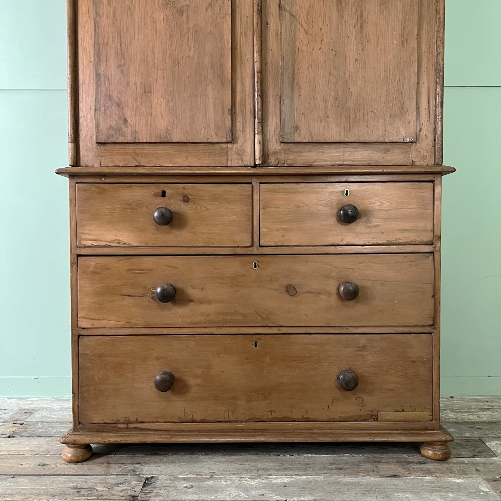 An antique Victorian pine cupboard on chest featuring a top section with two arched panel doors above three drawers with turned wooden handles. View III