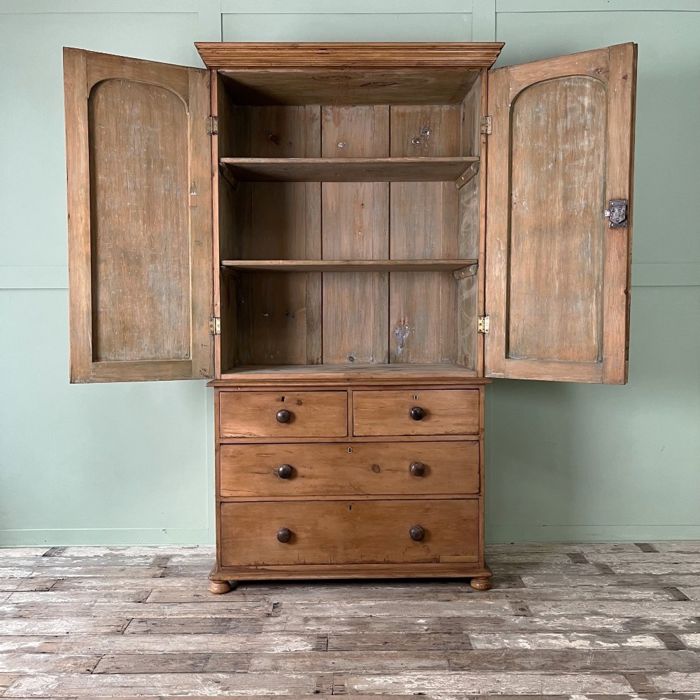An antique Victorian pine cupboard on chest featuring a top section with two arched panel doors above three drawers with turned wooden handles. View IV