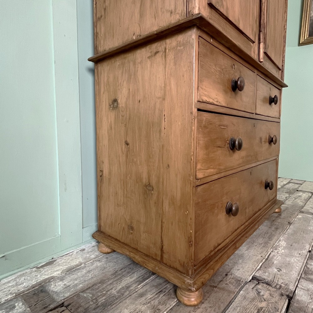 An antique Victorian pine cupboard on chest featuring a top section with two arched panel doors above three drawers with turned wooden handles. View V