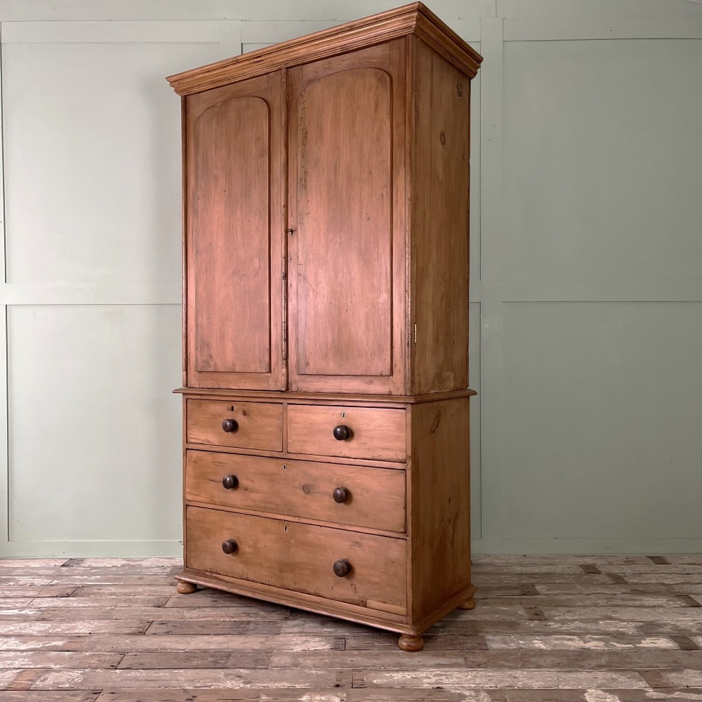 An antique Victorian pine cupboard on chest featuring a top section with two arched panel doors above three drawers with turned wooden handles. View X
