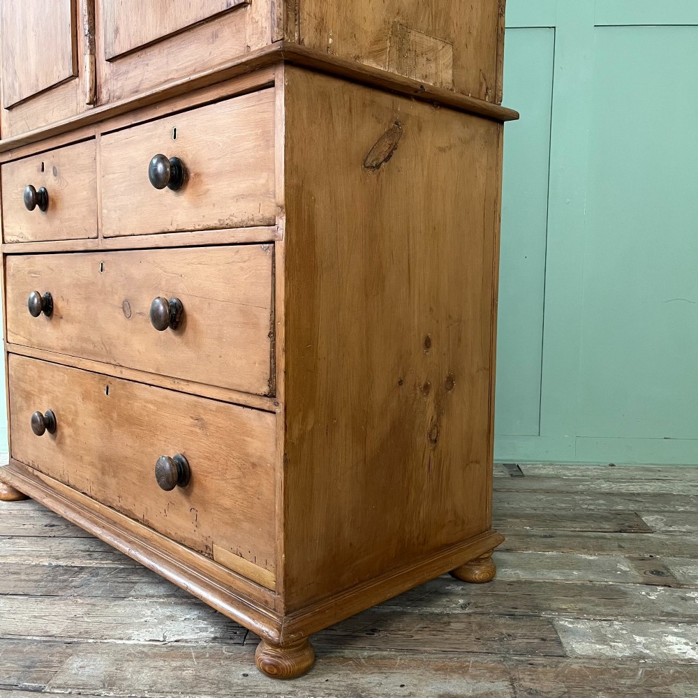 An antique Victorian pine cupboard on chest featuring a top section with two arched panel doors above three drawers with turned wooden handles. View XII