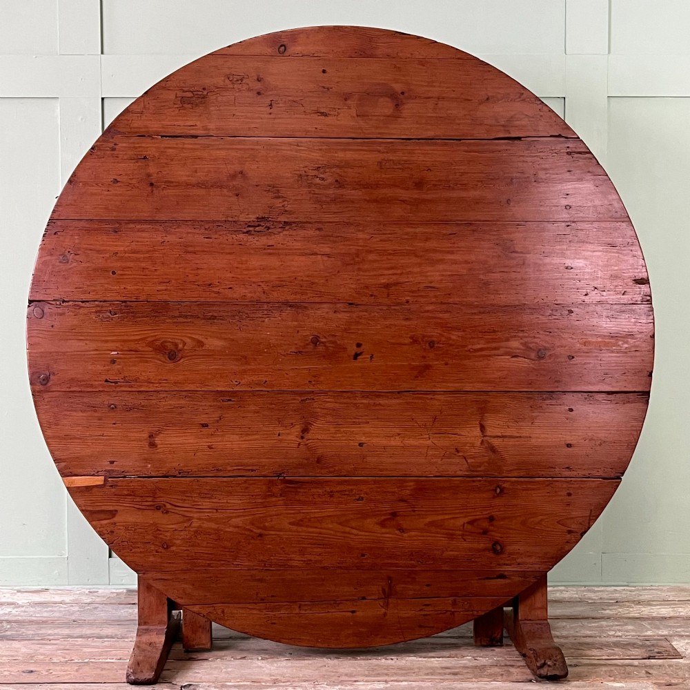 A 19th-century French circular tilt-top vendange table constructed from warm brown planked timber, shown tilted upright against a pale green wall. View II