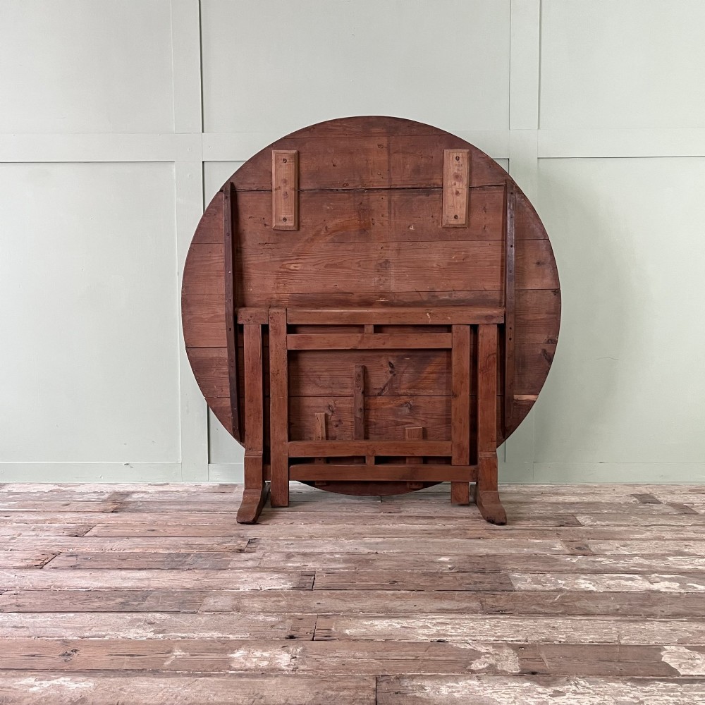 A 19th-century French circular tilt-top vendange table constructed from warm brown planked timber, shown tilted upright against a pale green wall. View V