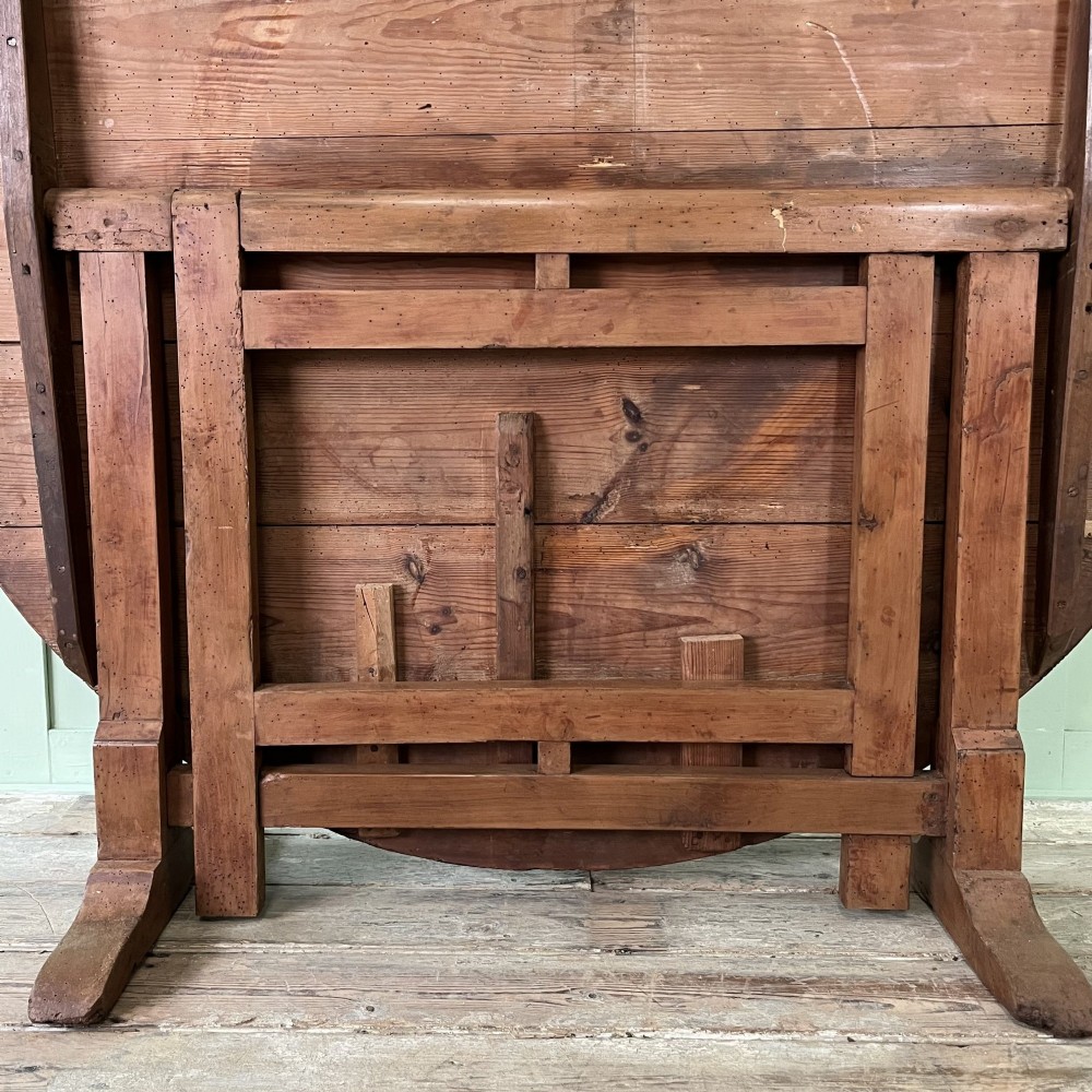 A 19th-century French circular tilt-top vendange table constructed from warm brown planked timber, shown tilted upright against a pale green wall. View VI
