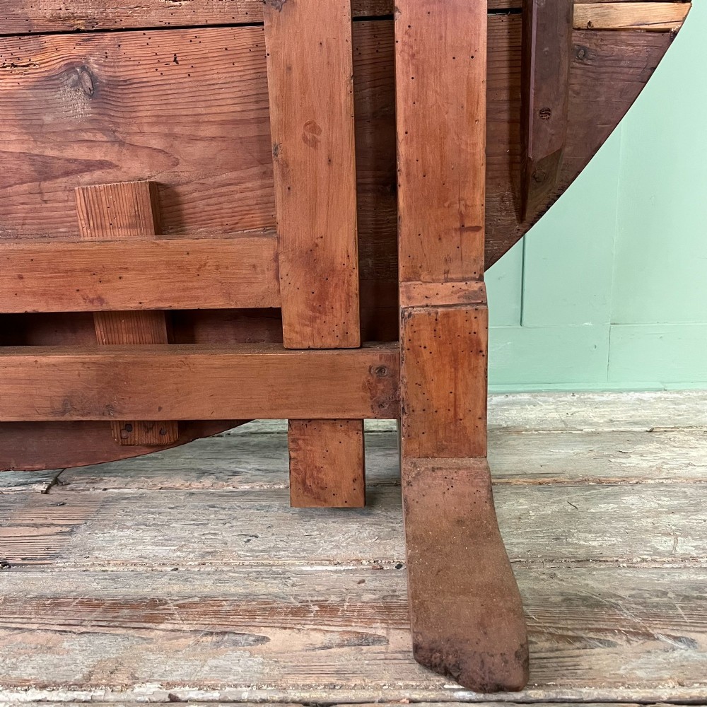 A 19th-century French circular tilt-top vendange table constructed from warm brown planked timber, shown tilted upright against a pale green wall. View VII